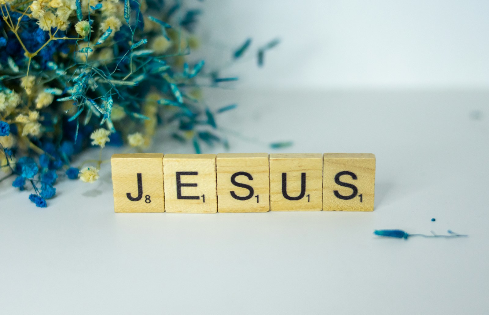 Photo by Alex Shute a wooden block spelling jesus next to a bouquet of flowers