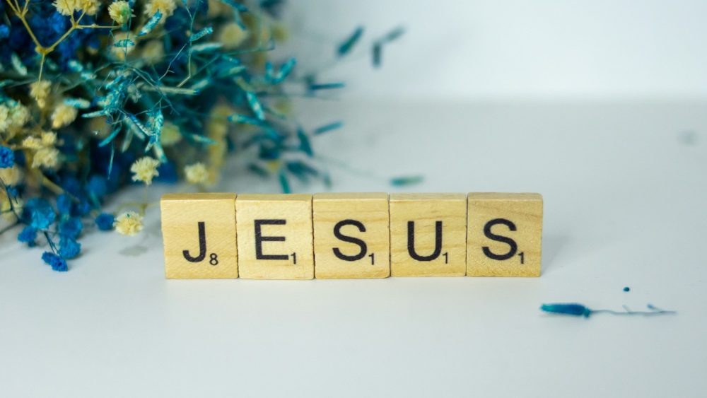 a wooden block spelling jesus next to a bouquet of flowers